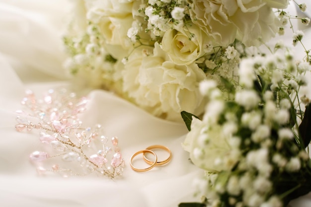 Wedding rings and jewelry on a white translucent calico fabric next to a bouquet of flowers