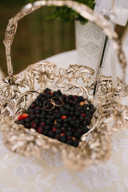 Wedding rings lie in a basket with berries - blueberries, in front of a field recording of the newlyweds, wedding rustic, selective focus