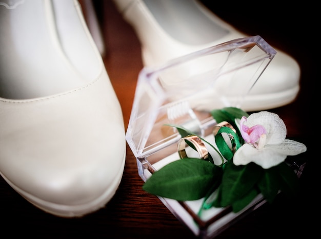 Wedding rings lie in glass box with flowers before silky shoes