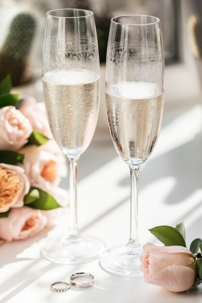 Wedding rings lie next to two glasses of champagne and a bouquet of roses