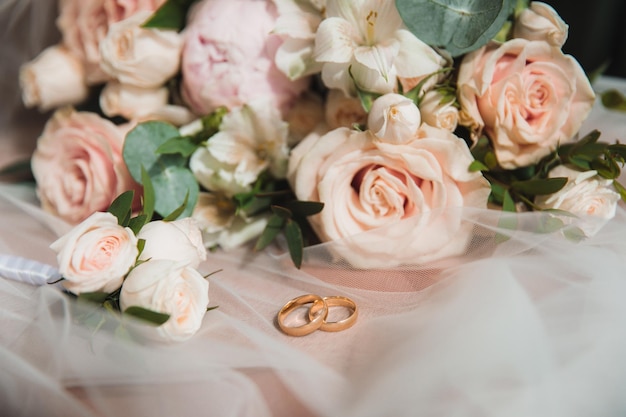 Wedding rings lie on the veil against the background of the bride's bouquet