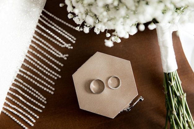 Wedding rings lie on a wooden box next to the bride's bouquet