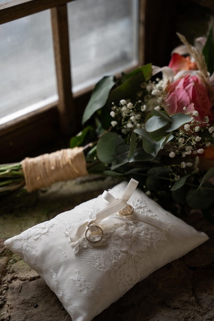 wedding rings on a pillow, a bouquet of flowers in the background and a window, jewelry