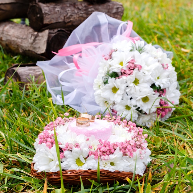 Wedding rings on a stand and a bridal bouquet of white chamomiles on a green grass. Selective focus.