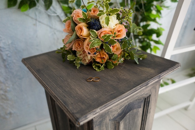 Wedding rings on a tinted wooden pedestal on the background of a stylish wedding bouquet