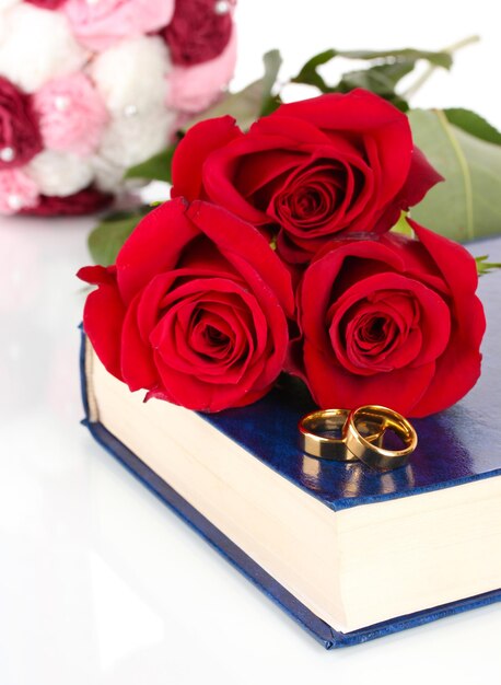 Wedding rings with roses on bible isolated on white