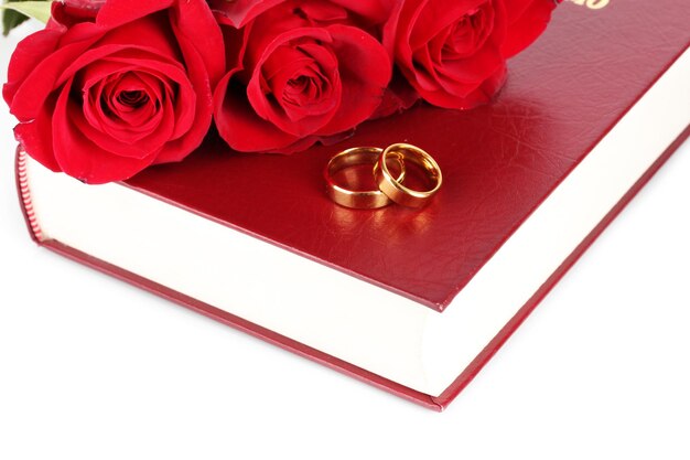 Wedding rings with roses on bible isolated on white