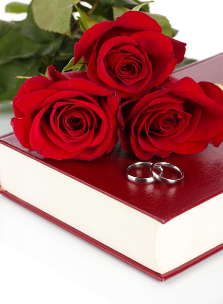 Wedding rings with roses on bible isolated on white