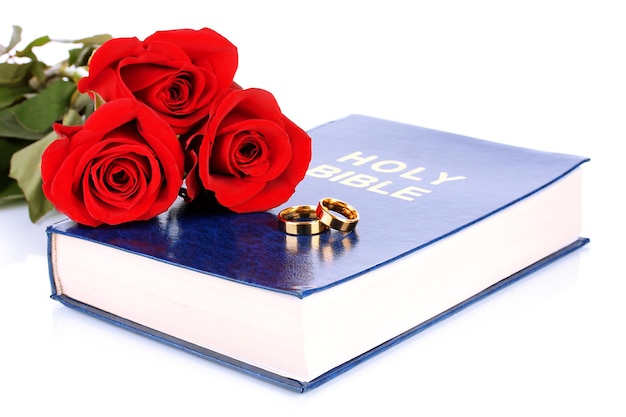 Wedding rings with roses on bible isolated on white