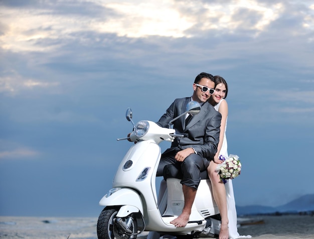 Foto scena del matrimonio degli sposi appena sposati sulla spiaggia, giro in scooter bianco e divertirsi