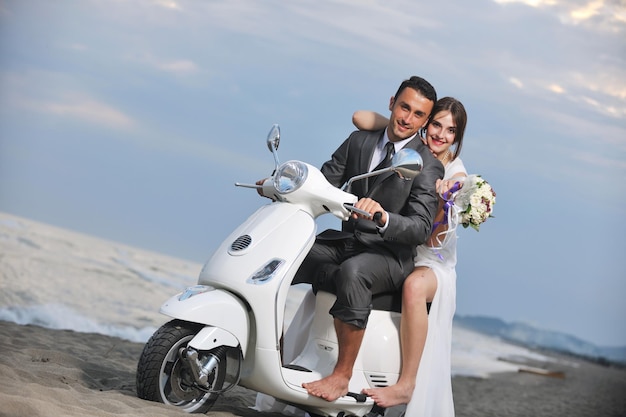 Foto scena del matrimonio degli sposi appena sposati sulla spiaggia, giro in scooter bianco e divertirsi