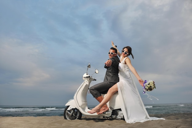 Scena del matrimonio degli sposi appena sposati sulla spiaggia, giro in scooter bianco e divertirsi