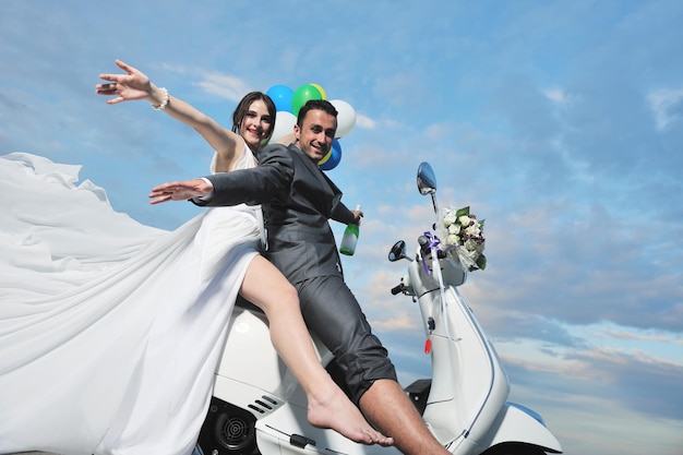 Foto scena del matrimonio degli sposi appena sposati sulla spiaggia, giro in scooter bianco e divertirsi