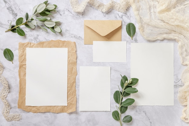 Wedding stationery set with envelope laying on a marble table decorated with eucalyptus branches and ribbons. Mock-up scene with blank paper greeting cards. Feminine flat lay