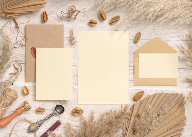Wedding suite cards and envelopes near dried plants, palm leaves and pampas grass top view. Boho scene with blank paper cards flat lay. Wedding set cards mockup, place for text