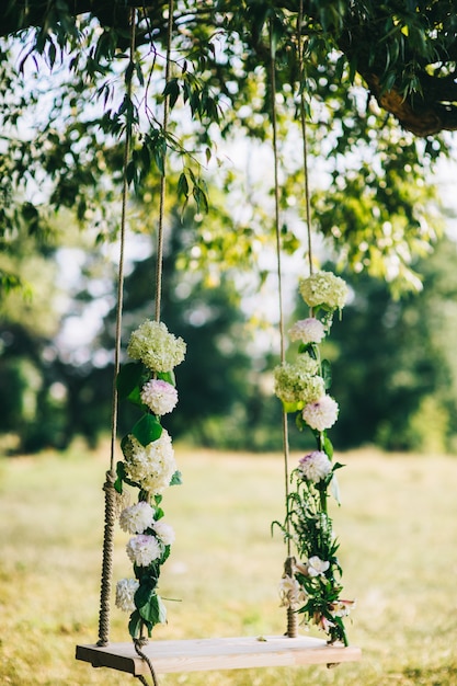 Wedding swing decorated with flowers hanging on the branches of the old willow