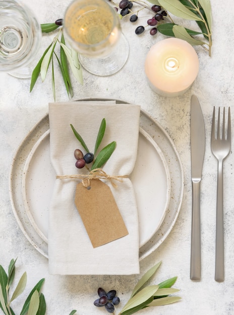 Wedding Table place with a place card and porcelain plates decorated with olive branches top view. Elegant modern template with horizontal blank paper card. Mediterranean flat lay mockup, copy space