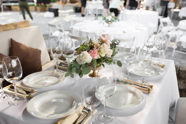 Сервировка свадебного стола украшена живыми цветами в латунной вазе.