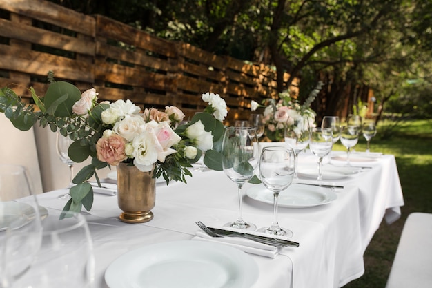 Сервировка свадебного стола украшена живыми цветами в медной вазе