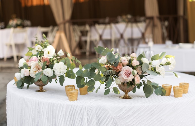 Фото Сервировка свадебного стола украшена живыми цветами в латунной вазе.