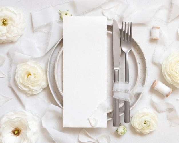 Фото Сервировка свадебного стола с открыткой рядом с кремовыми розами и белыми шелковыми лентами, макет сверху
