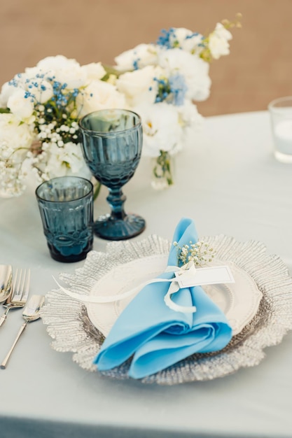 プレミアムグラスと花で飾られた青いテーブルクロスを持つゲストのための結婚式のテーブル