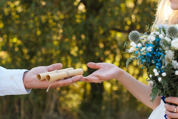 Wedding vowes on rolled paper sheet on groom palm, wedding bouquet, rustic outdoor wedding concept.