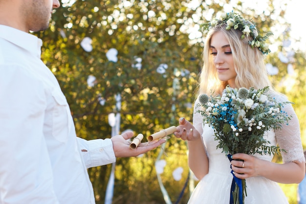 Wedding vowes on rolled paper sheet on groom palm, wedding bouquet, rustic outdoor wedding concept.