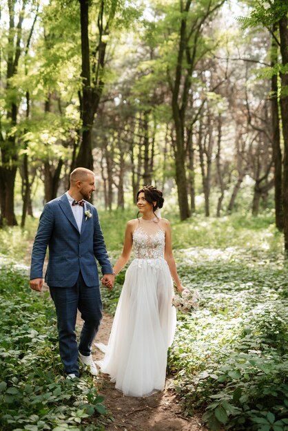 Wedding walk of the bride and groom in the deciduous forest in summer