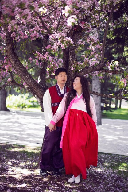 Il giovane uomo di nozze e una donna coreana in costumi nazionali stanno vicino all'albero dei fiori di ciliegio in primavera