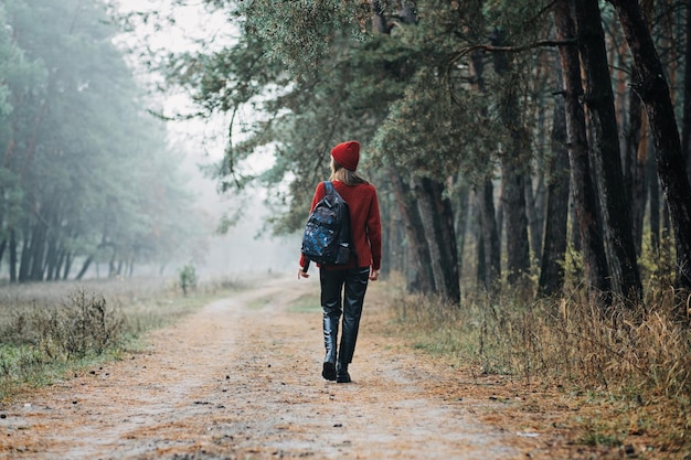 週末の休憩や森での休暇は自然の近くにとどまる赤い帽子とセーターを着た若い女性