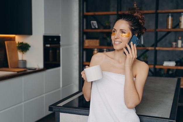 Weekend morning phone talk Young woman applies anti wrinkle eye patches and talking on phone