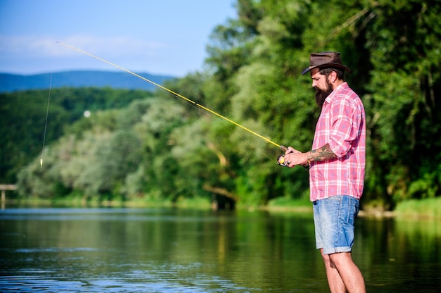 Weekend relax mature bearded man with fish on rod hipster fishing with spoonbait fly fish hobby Summer fishery activity successful fisherman in lake water big game fishing relax on nature