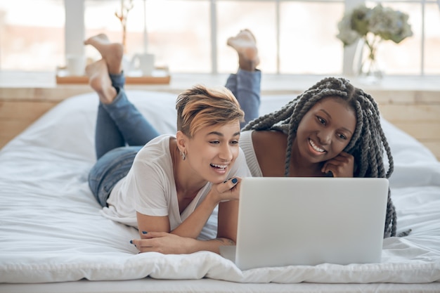 Weekend. Two girls lying on the bed and watching a movie on a laptop