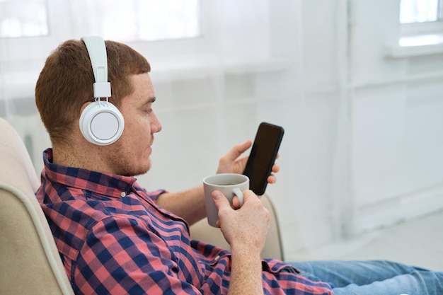 Weekend vibes young redhead engrossed in music and podcasts on his smartphone rise of online audio