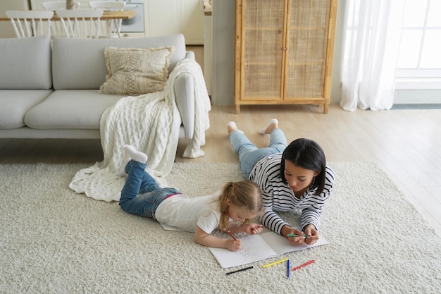 Foto weekendochtend van familie moeder en kind die samen op de vloer liggen en schilderen met kleurrijke stiften