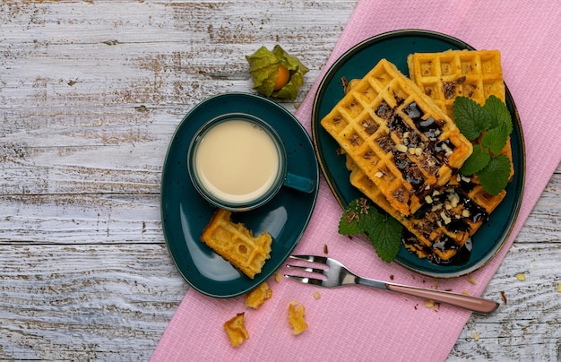 Weense wafels met chocoladesuikerglazuur op een donkerblauwe schotel op een lichte houten ondergrond een kopje room