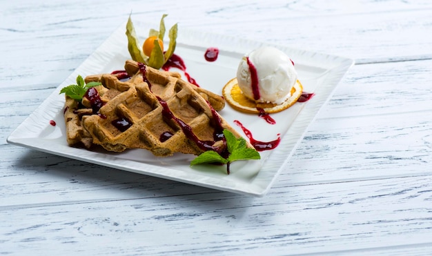 Weense wafels met roomijs en stroop op een witte plaat en op een witte houten ondergrond