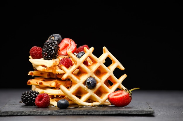 Weense wafeltjes met bessen die honing op zwarte achtergrond gieten