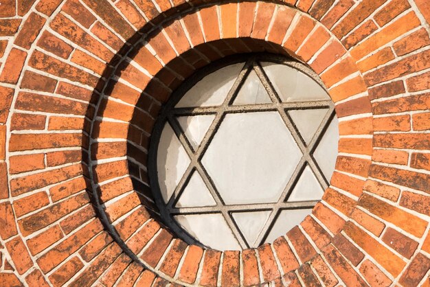 Weergave van een pentagram teken en symbool op een oud rond raam op een rode bakstenen muur Vintage glas met metalen frame en vijfhoek op historisch kerkgebouw en achtergrond Architectuur circulaire ontwerp