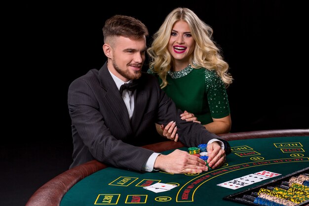 Weergave van jonge, zelfverzekerde man met de dame terwijl hij pokerspel speelt. De blondine kijkt in de camera en lacht