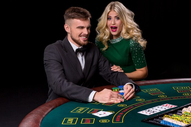 Weergave van jonge, zelfverzekerde man met de dame terwijl hij pokerspel speelt. De blondine kijkt in de camera