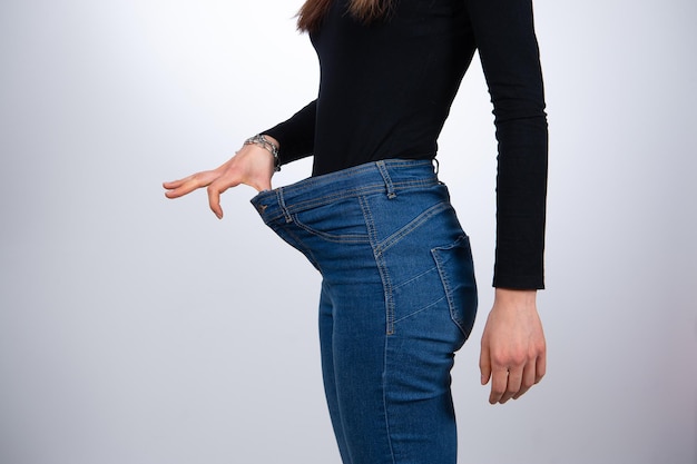 Weergave van slanke taille van aantrekkelijke vrouw in grote jeans nadruk op haar succes in gewichtsverlies geïsoleerd op een witte achtergrond Dieet concept kopie ruimte