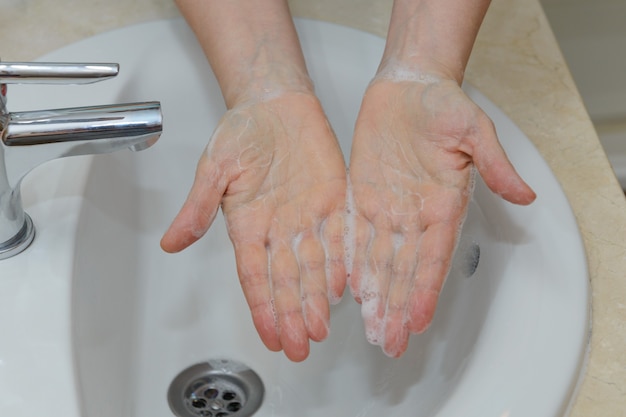 Weergave van vrouwelijke handen in zeepachtig schuim onder leidingwater close-up