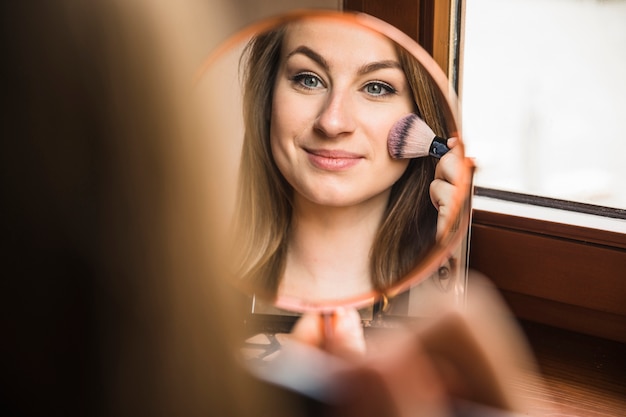 Weerspiegeling van een mooie vrouw die make-up op haar gezicht doet