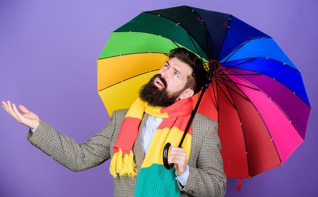 Weersvoorspellingsconcept Man met baard en hipster houdt kleurrijke paraplu vast Het lijkt te regenen Regenachtige dagen kunnen moeilijk zijn om door te komen Voorbereid op regenachtige dag Zorgeloos en positief Geniet van regenachtige dag