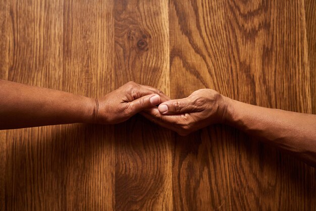 Wees er altijd voor elkaar Hoge hoekopname van een onherkenbaar senior koppel dat de handen bij elkaar houdt boven een houten tafel thuis