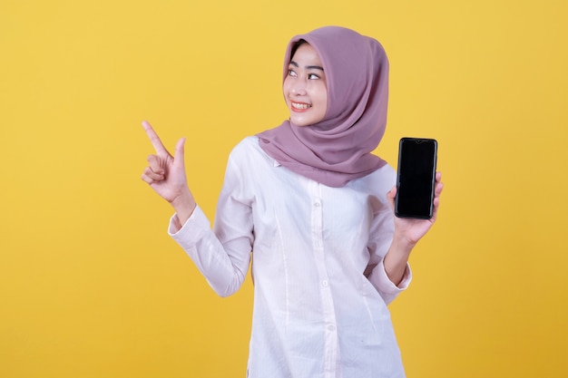 Wees slim, koop dit apparaat, portret van jonge Aziatische vrouw die hardop lacht, hijab draagt die naar boven wijst en het apparaatscherm toont