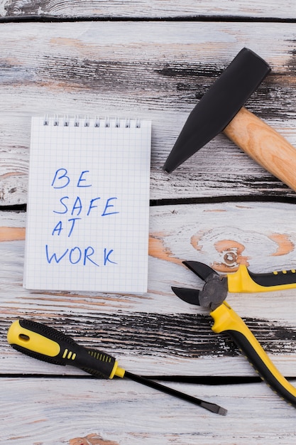 Wees veilig op het werk slogan en hulpmiddelen voor reparatie of construtcing. Bovenaanzicht hamer met lagen en schroevendraaier op wit hout.