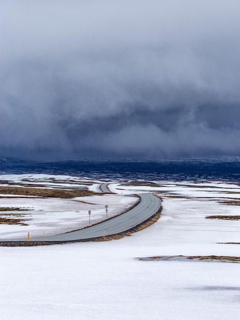 Weg door land bedekt met sneeuw en ijs met donkere wolken op de achtergrond